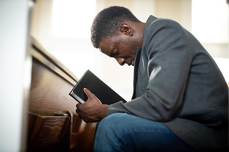 ADF Client, Chike Uzuegbunam praying in church while holding a Bible