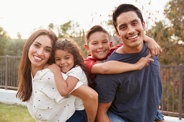 Young Hispanic parents piggyback their children in the park