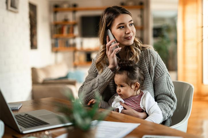 Young Mother Holding Infant While On The Phone 