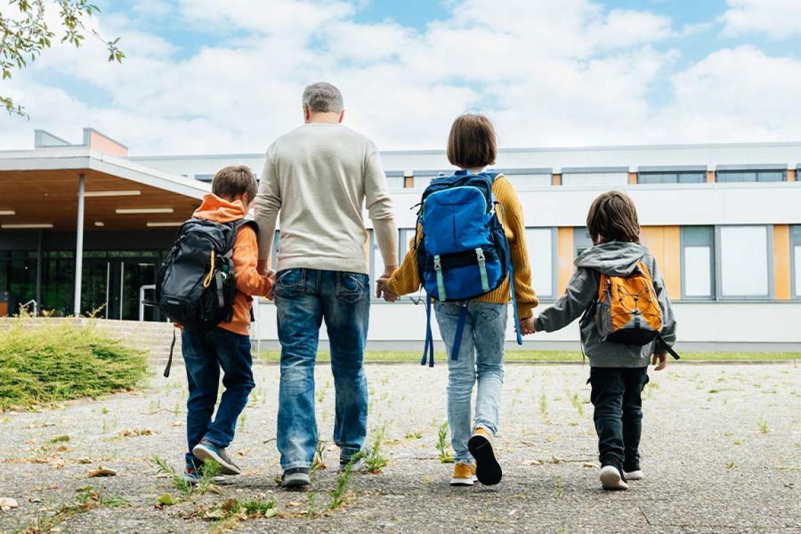 Father and children with backpacks walking to school